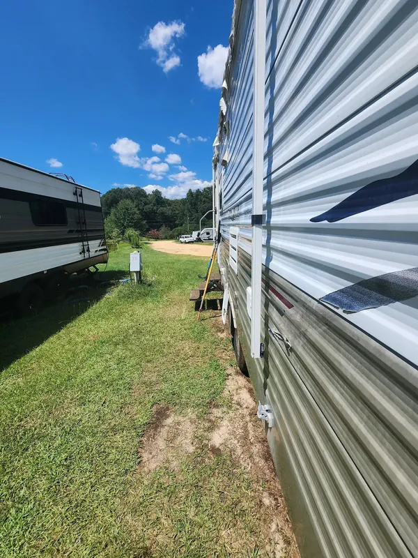 A travel trailer on a grassy site with its utility pedestal under a blue sky