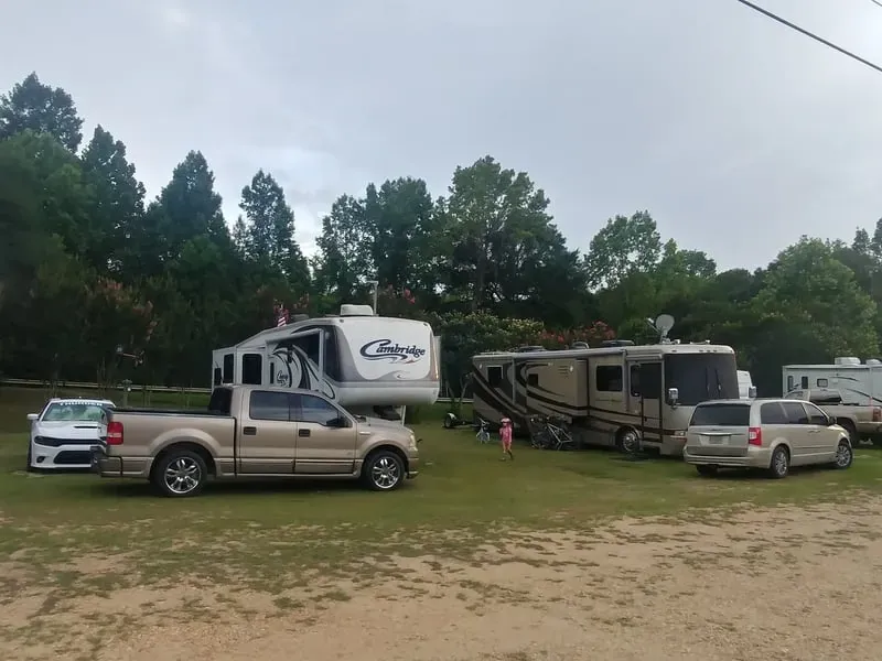 Fifth-wheel and motorhome parked on grassy sites under tall shade trees